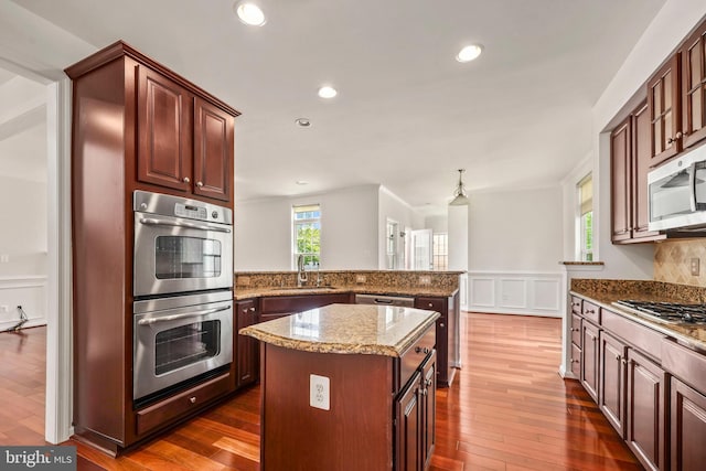 kitchen with a peninsula, a decorative wall, a wainscoted wall, light stone counters, and stainless steel appliances