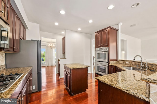 kitchen featuring dark wood-style flooring, light stone counters, appliances with stainless steel finishes, a sink, and a center island