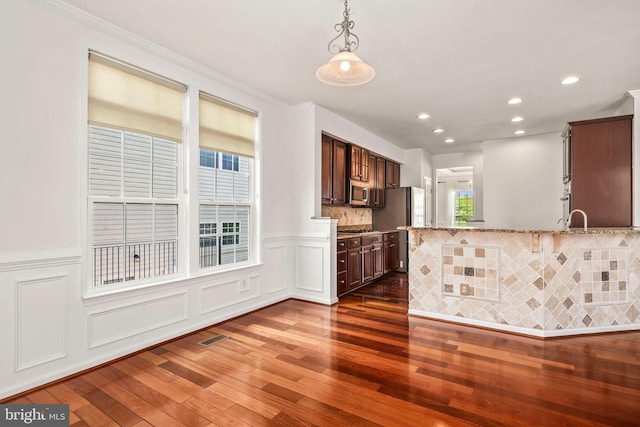 kitchen featuring light stone countertops, dark brown cabinets, dark wood finished floors, decorative light fixtures, and stainless steel appliances