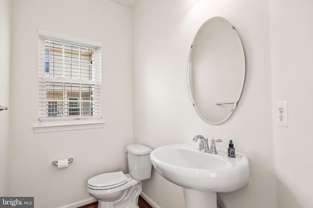 half bath with toilet, baseboards, and a sink