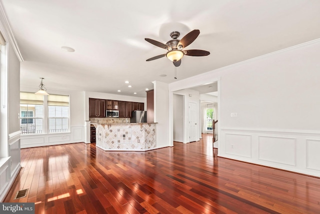 unfurnished living room with crown molding, ceiling fan, a decorative wall, dark wood-type flooring, and visible vents