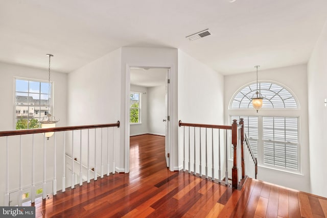 hallway featuring a healthy amount of sunlight, visible vents, wood-type flooring, and an upstairs landing