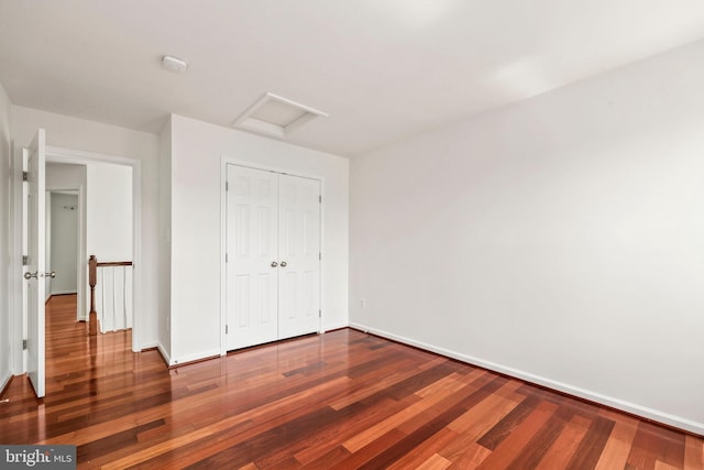 unfurnished bedroom featuring baseboards, attic access, and wood finished floors