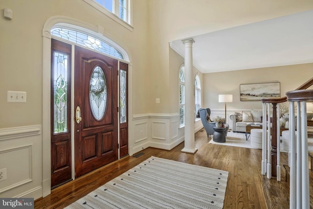 entryway featuring a decorative wall, ornate columns, wood finished floors, and a wainscoted wall
