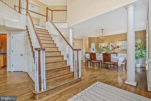 staircase with ornamental molding, decorative columns, a towering ceiling, and wood finished floors