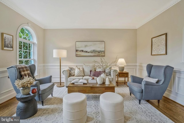 living area featuring crown molding, wainscoting, wood finished floors, and a decorative wall