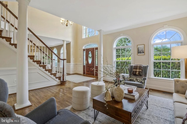 living room with a decorative wall, stairs, decorative columns, wood finished floors, and ornamental molding
