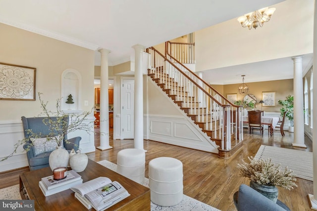 living room featuring ornamental molding, ornate columns, wood finished floors, and a notable chandelier