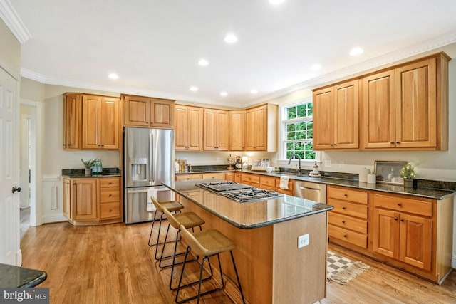kitchen featuring a kitchen bar, a center island, ornamental molding, stainless steel appliances, and light wood-style flooring