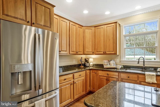 kitchen with ornamental molding, stainless steel fridge, recessed lighting, a sink, and dark stone countertops