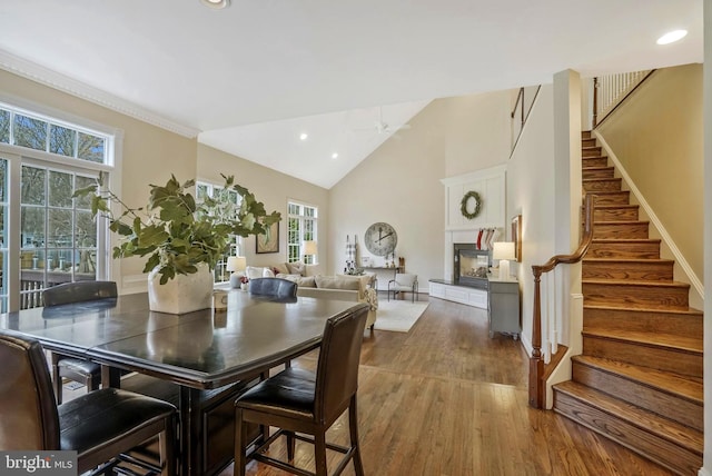 dining area with a fireplace with raised hearth, a healthy amount of sunlight, wood finished floors, and stairway