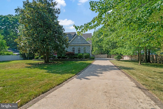 obstructed view of property featuring fence, a front lawn, and stone siding