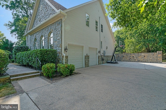 view of side of property with a garage, stone siding, and concrete driveway