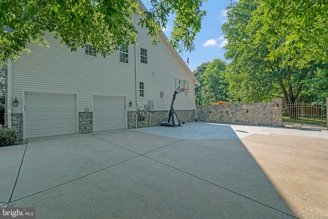 view of side of property featuring fence, a garage, driveway, and stone siding