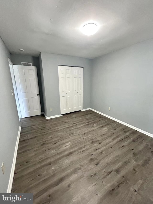 unfurnished bedroom featuring baseboards, dark wood-style floors, a closet, and visible vents