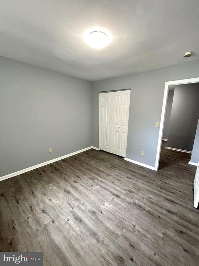 unfurnished bedroom featuring baseboards, dark wood-style floors, and a closet