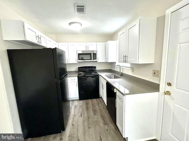 kitchen featuring light wood-style flooring, a sink, visible vents, white cabinets, and black appliances