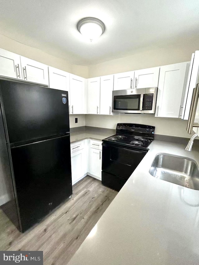 kitchen featuring light countertops, a sink, light wood finished floors, white cabinetry, and black appliances