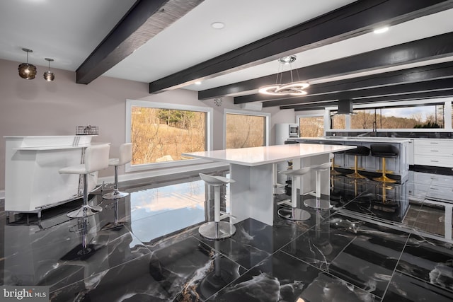 kitchen featuring marble finish floor, a breakfast bar, beam ceiling, and an inviting chandelier