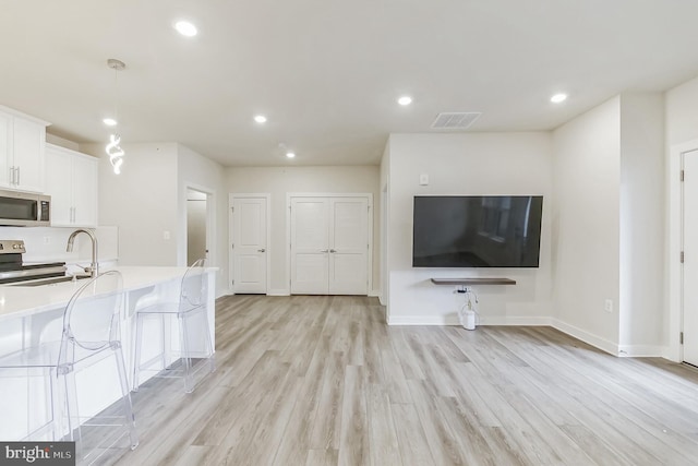 kitchen featuring light countertops, light wood finished floors, appliances with stainless steel finishes, white cabinetry, and a sink