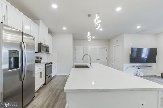 kitchen with light wood finished floors, a center island with sink, appliances with stainless steel finishes, white cabinetry, and a sink