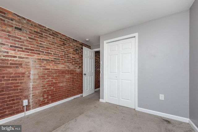2110 E Hoffman St, Baltimore, MD 21213 - unfurnished bedroom featuring baseboards, a closet, carpet floors, and brick wall