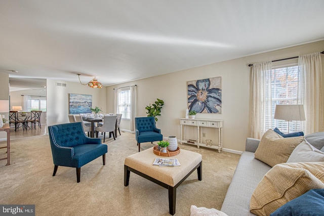 living area with baseboards, visible vents, light colored carpet, and a notable chandelier