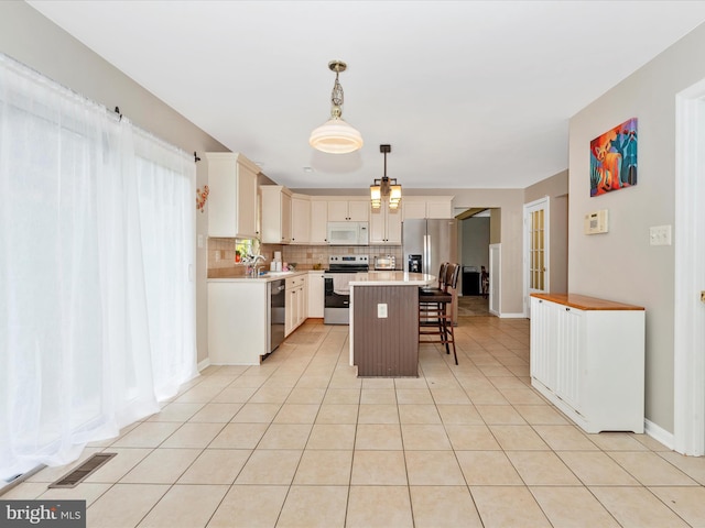 kitchen featuring tasteful backsplash, visible vents, light countertops, stainless steel appliances, and a breakfast bar area