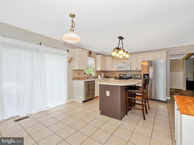 kitchen featuring tasteful backsplash, visible vents, a kitchen island, stainless steel appliances, and decorative light fixtures