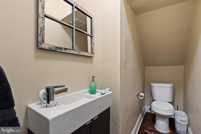 half bath featuring toilet, vanity, wood finished floors, and baseboards