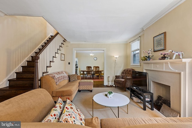 carpeted living room featuring a fireplace, stairway, and crown molding