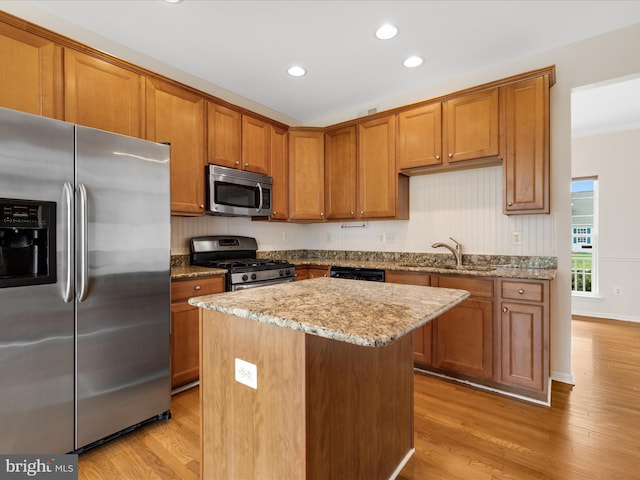 kitchen featuring stainless steel appliances, a sink, light stone counters, light wood-style flooring, and brown cabinets