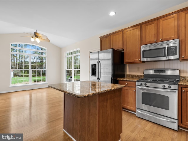 kitchen with brown cabinets, a kitchen island, appliances with stainless steel finishes, dark stone countertops, and lofted ceiling