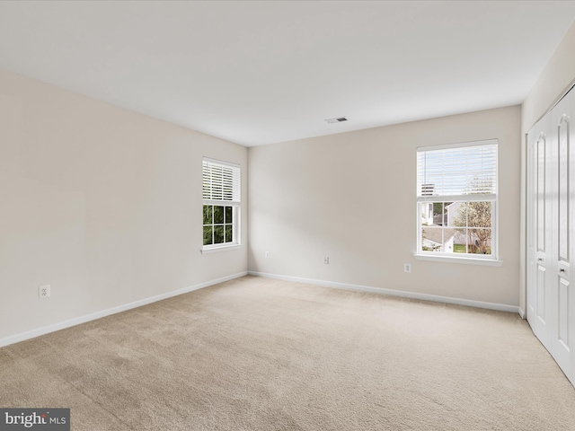 spare room with baseboards, a healthy amount of sunlight, light colored carpet, and visible vents