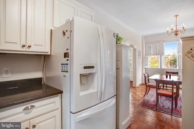kitchen with crown molding, white refrigerator with ice dispenser, white cabinets, dark stone countertops, and a notable chandelier