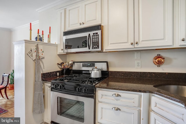 kitchen with ornamental molding, dark stone countertops, stainless steel gas stove, and white cabinetry
