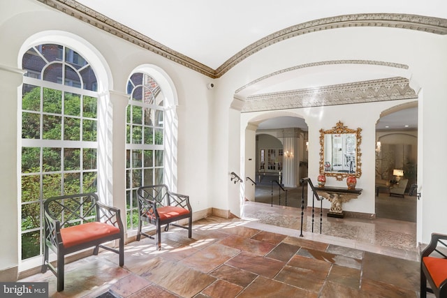 interior space with arched walkways, baseboards, decorative columns, and stone tile flooring