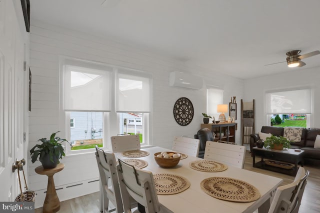 dining area with a wall mounted AC, wood finished floors, and ceiling fan
