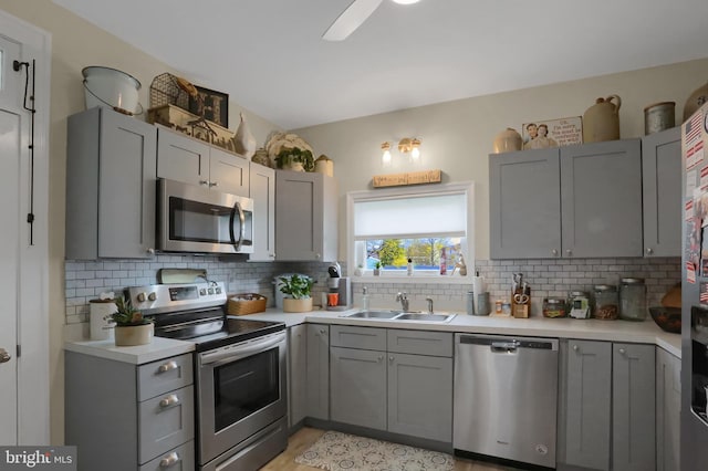 kitchen featuring a sink, gray cabinets, light countertops, backsplash, and appliances with stainless steel finishes