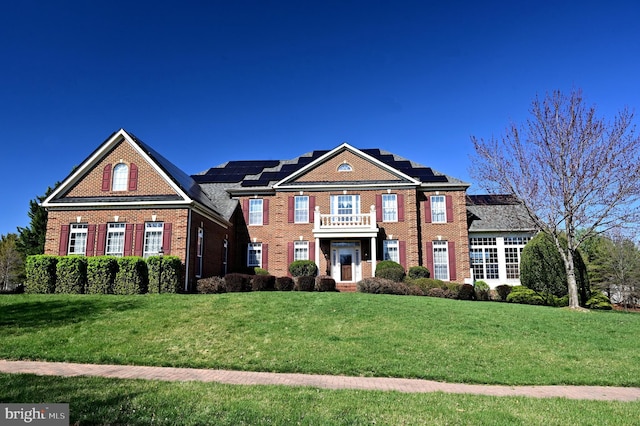 colonial house featuring brick siding, roof mounted solar panels, and a front yard