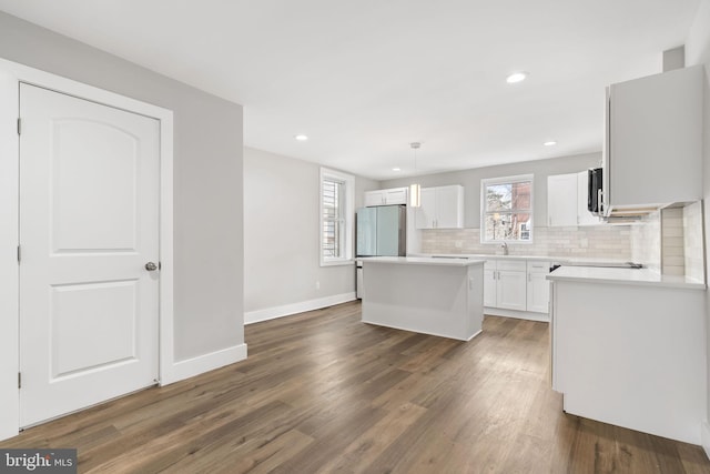 kitchen with freestanding refrigerator, a center island, white cabinets, decorative backsplash, and dark wood-type flooring