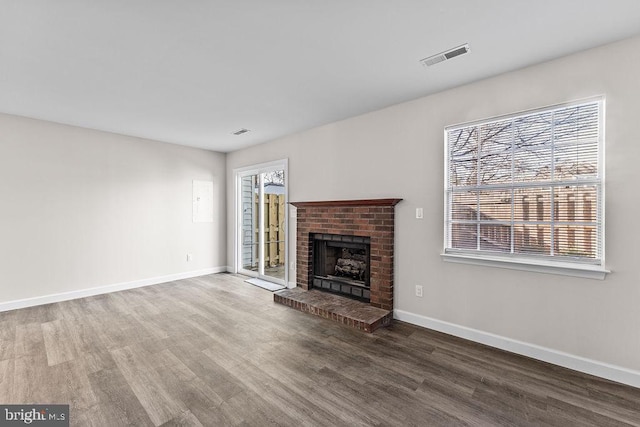 unfurnished living room with baseboards, visible vents, a brick fireplace, and wood finished floors