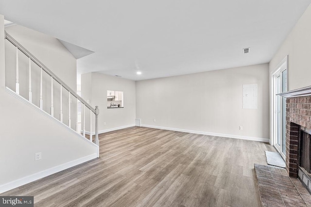 unfurnished living room with stairway, a fireplace, wood finished floors, baseboards, and visible vents