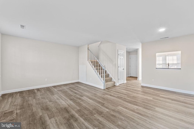 unfurnished living room with baseboards, visible vents, wood finished floors, and stairway