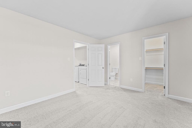 unfurnished bedroom featuring washing machine and clothes dryer, a closet, baseboards, a walk in closet, and light colored carpet