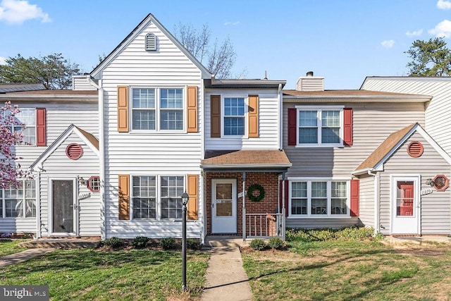 townhome / multi-family property featuring a chimney, a front yard, and brick siding