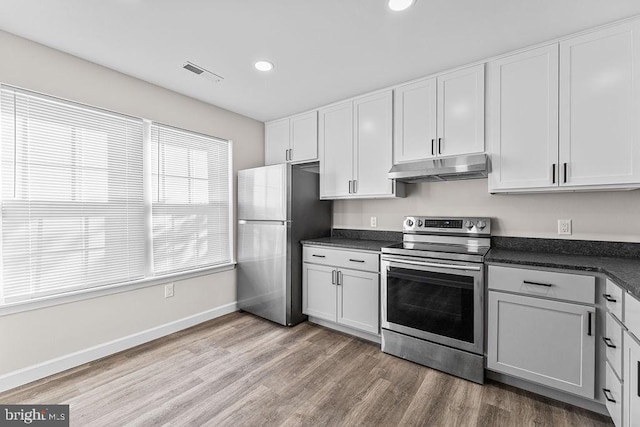 kitchen with white cabinetry, wood finished floors, under cabinet range hood, stainless steel appliances, and dark countertops