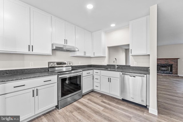 kitchen featuring stainless steel appliances, dark countertops, under cabinet range hood, white cabinetry, and a sink