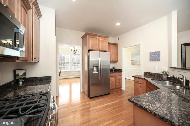 kitchen featuring light wood finished floors, appliances with stainless steel finishes, dark stone countertops, a sink, and brown cabinetry