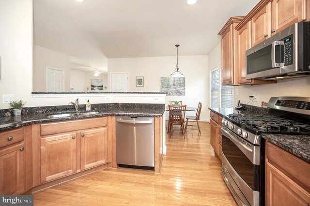 kitchen with a sink, dark stone counters, light wood-type flooring, and appliances with stainless steel finishes